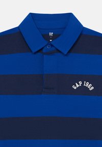 Μπλε και ναυτικό πουκάμισο polo με ρίγες, κολάρο, ένα κουμπί και λευκή κεντημένη γραφή "GAP 1969" στο στήθος.