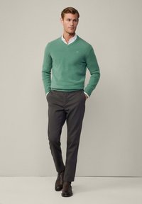 Grön ull v-ringad tröja, bärs över en vit skjorta med krage. Matchad med mörkgrå byxor och bruna läderstövlar. Enkel, figursydd design.