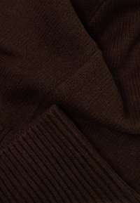 Hnědá pletenina s ribkovanou strukturou a měkkým, silným tkaním. Důraz na tmavý odstín a hladký povrch materiálu.