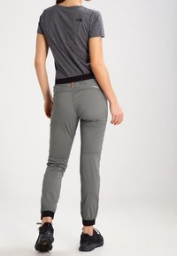 Šedé sportovní kalhoty se zúženým střihem a elastickými manžetami, doplněné černým pasem. Nahoře je nošeno šedé přiléhavé tričko.