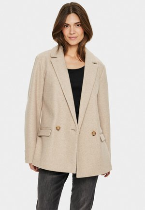 Blazer beige à double boutonnage en tissu doux, avec deux poches avant, des accents de boutons dorés et des revers crantés.