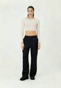 Top branco cropped de mangas longas combinado com calças largas pretas com riscas; tecido suave com brilho subtil, usado com sapatos chunky pretos.