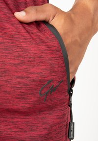 Rood heathered sportkleding met een ritszak, zwarte accenten en een logo. De stof lijkt zacht met een gestructureerde afwerking.