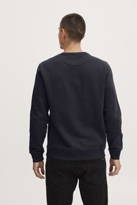 Sudadera de algodón azul marino con cuello redondo, mangas largas y puños de canalé. La parte posterior presenta una textura suave con un detalle mínimo.