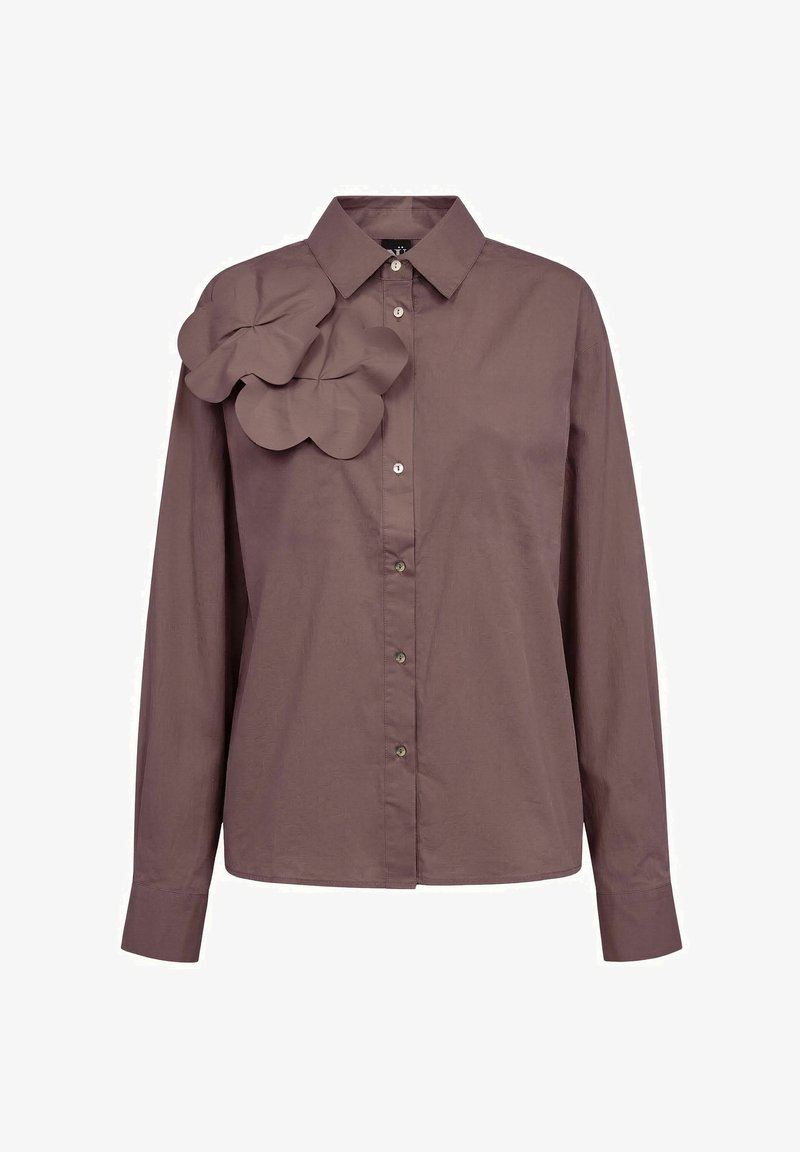 Chemise marron à manches longues, boutonnée, avec col et deux grandes applications de fleurs en tissu sur l’épaule gauche.