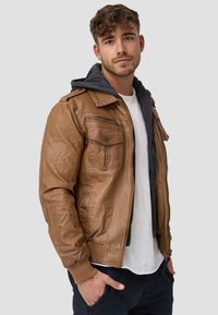 Veste aviateur en cuir marron avec fermeture éclair à l'avant, poches poitrine doubles et capuche grise. Texture douce et design décontracté, idéale pour le superposition.