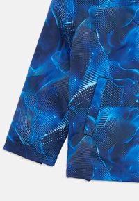 Manche de veste bleue et section inférieure avec un motif de vague numérique abstrait dans des tons de bleu clair et de blanc, et une poche latérale.