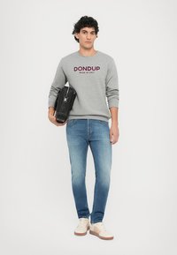Pelēks džemperis ar uzrakstu "DONDUP MADE IN ITALY", zili džinsi, gaiši sporta apavi un melna plecu soma. Modelis stāv uz baltā fona.
