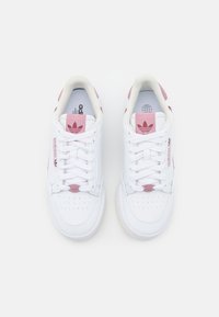 Sneaker bianche con accenti rosa, tomaia in pelle liscia, punta rotonda, dettagli perforati e lacci piatti. Logo Adidas sulla linguetta e sul lato.