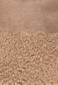 Tissu beige avec une texture tricotée lisse sur le dessus et une texture en peluche bouclée et douce en dessous.