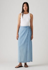 Lys blå denim omslagskjørt med en bindedetalje, ankel-langt, båret over en hvid ærmeløs top og parret med sorte flade sandaler.