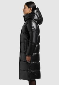 Crni dugi puhasti kaput sa sjajnim završetkom, kapuljačom, džepovima na patentni zatvarač i prošivenim dizajnom. Ima logo na rukavu i podesivu kapuljaču.