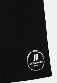 Zwarte katoenen T-shirt hoek met wit rond logo. De tekst bevat "RESEARCH_DESIGN_APPAREL" en "JACK&JONES." Gladde textuur, getailleerd ontwerp.