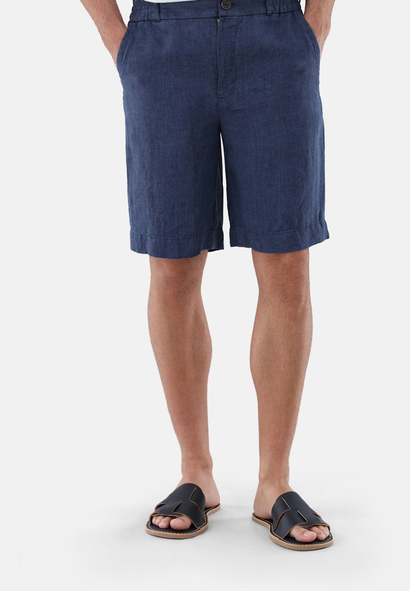 Navy Leinen Shorts mit Knopfverschluss und Seitentaschen, die einen lockeren Schnitt und umgeschlagene Säume aufweisen, kombiniert mit schwarzen Schlüpfschuhen.
