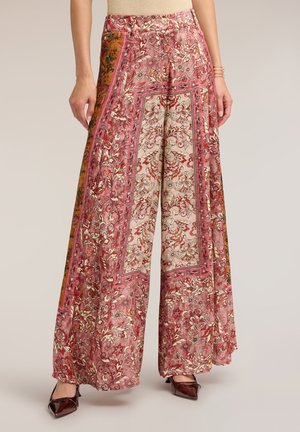 Pantaloni a gamba larga con motivi floreali e paisley rosa e rossi, abbinati a scarpe scure con punta affilata e top beige.