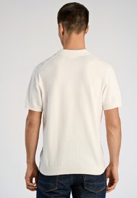 Λευκό πλεκτό πόλο με κοντά μανίκια, άνετη εφαρμογή, ριμπ γιακά και πλευρικές σχισμές στο τελείωμα. Ομαλή υφή, μινιμαλιστικός σχεδιασμός.