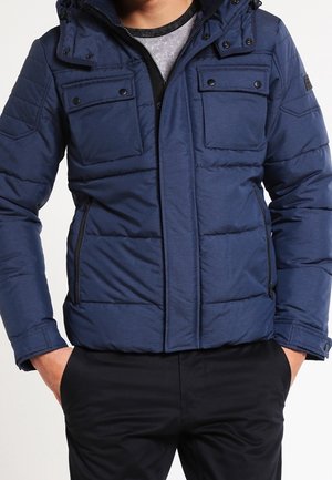 Navy blue padded jacket with a hood, featuring two chest pockets and side zippers, made from a smooth fabric with a subtle sheen.