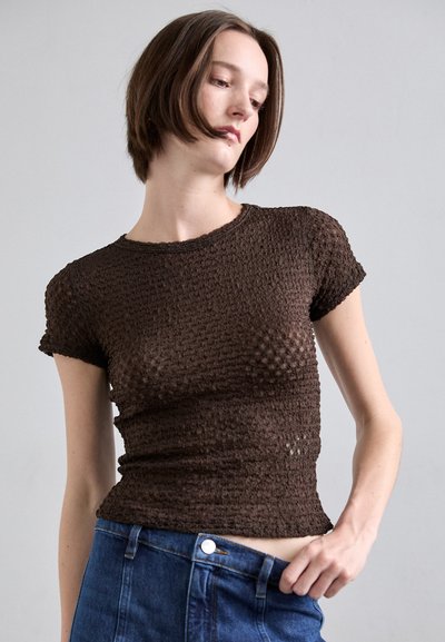 Hnědý pletený tričko s texturovaným vzorem, krátkými rukávy a kulatým výstřihem, spárované s džínami s vysokým pasem.