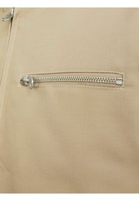 Beige stof met een gestructureerd oppervlak heeft een ritszak, met zilveren hardware en een soepele ritsbaan voor gemakkelijke toegang.