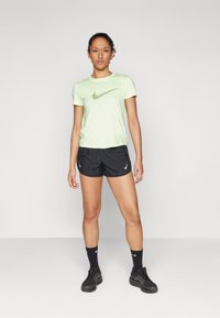 Lys grønn treningsskjorte med grå Nike-logo, parret med svarte shorts med hvit Nike-logo, svarte sokker og mørke joggesko.