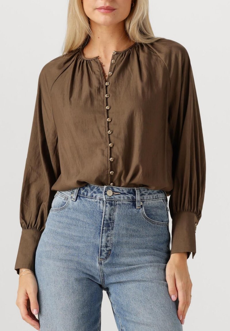 Bruine blouse met lange mouwen en een ronde hals, voorzien van een knoopsluiting aan de voorkant met decoratieve knopen en gecentreerde mouwen, gecombineerd met blauwe hoge taille jeans.