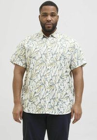 Camisa de botón de manga corta en tejido ligero con un patrón de hojas amarillas y azules sobre un fondo blanco. Cuello clásico y corte relajado.