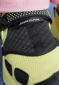 Svart og gul sneaker med en teksturert mesh-overdel, polstret stropp og merkevare. Fremtredende prikkete detaljer på kragen.