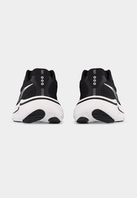 Ζευγάρι αθλητικών παπουτσιών τρεξίματος σε μαύρο και άσπρο, εμφανιζόμενα από πίσω σε απλό λευκό φόντο, που αναδεικνύουν τις παχιές σόλες και το σχεδιασμό της φτέρνας τους.