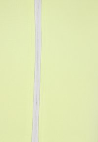 Lichtgeel stof met een gladde textuur en een centrale witte ritssluiting. Geen patronen of accenten zichtbaar.