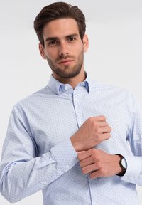 Camicia azzurro chiaro con piccoli pois blu navy, maniche lunghe e colletto. Presenta un design aderente e polsini regolabili.