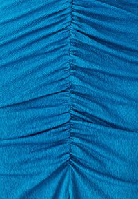 Tissu froncé en turquoise vif, présentant une texture verticale plissée, surface lisse avec une légère brillance, créant une apparence fluide.