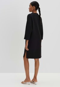 Black knee-length dress with 3/4 sleeves, side slits, and a relaxed fit. Smooth texture, minimal design, suitable for various occasions.