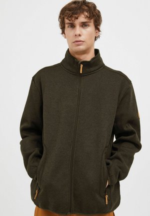 Mørkegrøn zip-up jakke med høj krave, sidelommer og tekstureret stof. Har træ-zippertræk og diskrete sømdetaljer.