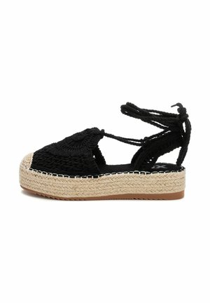 Espadrille negro tejido con punta redonda, suela intermedia de yute natural y lazos negros. Textura detallada en la parte superior y acentos decorativos.