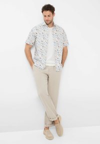 Short-sleeve floral shirt in white, featuring multicolored flower patterns, paired with light beige linen pants and slip-on beige shoes.