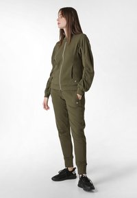Khaki zipová bunda s bočními kapsami a žebrovanými manžetami, spárovaná s odpovídajícími tepláky s elastickým pasem a zú�ženými nohavicemi.
