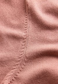 Záber zblízka na mäkkú ružovú pletenú tkaninu s detailným švom a jemnou rebrovanou štruktúrou, ukazujúcou jemné priadze a stehovú prácu.