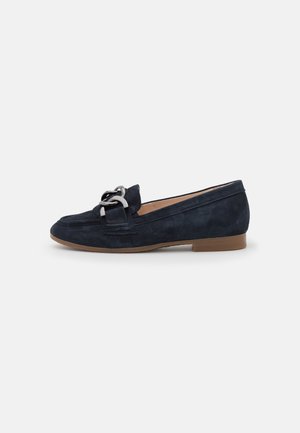 Mocassins en daim bleu marine avec une semelle plate, présentant un détail de quincaillerie en argent sur le devant. Texture lisse et design épuré.