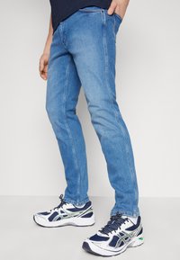 Lichtblauwe spijkerbroek met een slim fit, met contrasterende stiksels en een klassiek vijf-pocket ontwerp. Gecombineerd met witte en marineblauwe sneakers.