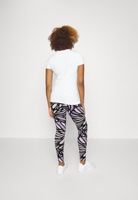 Witte t-shirt met korte mouwen gecombineerd met leggings met een zwart-paarse abstracte bladerenpatroon en witte sneakers.