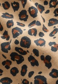Beige tyg med en texturerad yta som har svarta och bruna leopardmönster. Designen inkluderar olika storlekar av fläckar.