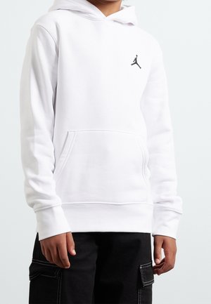 Kind draagt een witte capuchontrui met een klein zwart Jumpman-logo op de borst en zwarte cargobroek.