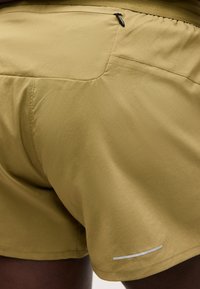 Κοντινή λήψη ταμπά αθλητικών σορτς με πίσω τσέπη με φερμουάρ και ανακλαστική λωρίδα στο τελείωμα, που φοριούνται από ένα άτομο.