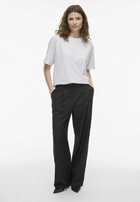 Camiseta blanca de mangas cortas combinada con pantalones anchos de talle alto de color negro. Los pantalones tienen pliegues y se complementan con tacones de punta.