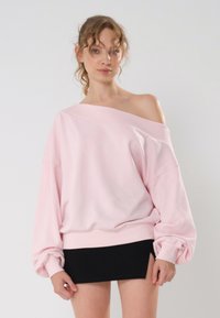 Felpa rosa off-shoulder con maniche lunghe a palloncino e polsini a costine. Abbinata a una mini gonna nera aderente. Texture liscia, design casual.