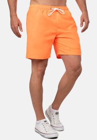 Pantaloni da bagno arancioni realizzati in materiale leggero, con una vita elastica dotata di un laccetto bianco e un dettaglio logo discreto.