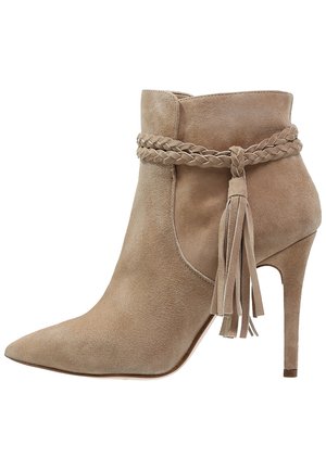 Beżowy zamszowy botek z zaostrzonym noskiem, plecionym zdobieniem wokół kostki i akcentem z chwostem, osadzony na obcasie typu szpilka.