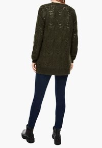 Grüner gestrickter Pullover mit strukturiertem Blattformmuster, langen Ärmeln und lockerer Passform, kombiniert mit dunkelblauen Skinny Jeans und schwarzen Knöchelstiefeln.