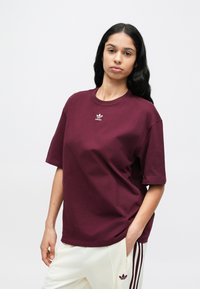 Bordó pamut póló kerek nyakkivágással, túlméretezett fazonnal és kis fehér hímzett logóval a mellkason. Sima textúra, rövid ujjú.