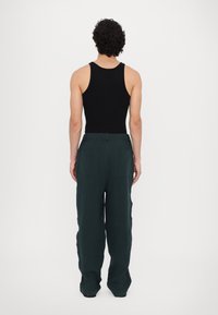 Black tank top and loose-fitting dark green pants. The pants feature a drawstring waist and two back pockets with a textured fabric.